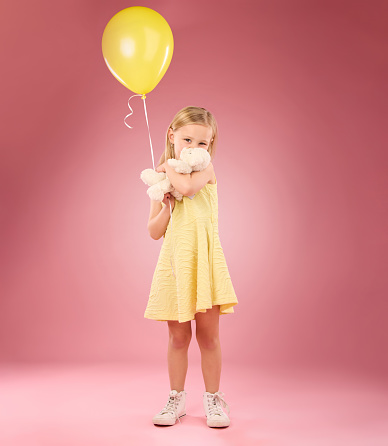 Teddy bear kiss, balloon and girl portrait with a soft toy with happiness and love for toys in a studio. Isolated, pink background and a young female child feeling happy, joy and cheerful with friend