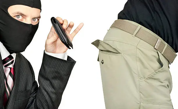 Close-up of a businessman wearing a balaclava picking the trouser pocket of a middle class man.