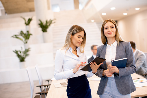 Two pretty young business women looking at financial results on digital tablet in front of their team at the office