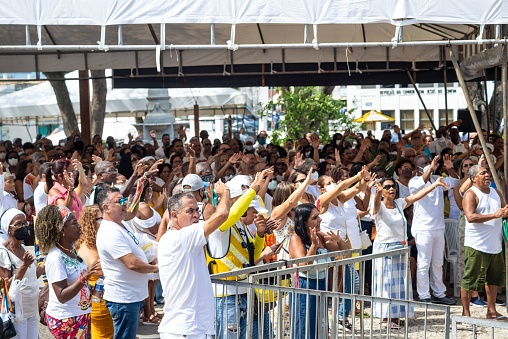 Salvador, Brazil – January 07, 2023: A diverse group of people is exhibiting a sense of joy and unity by raising their hands in celebration at a beach setting