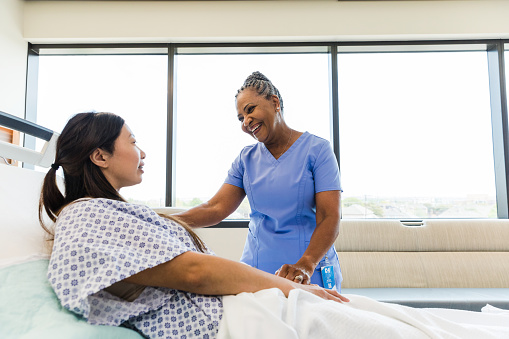 The mature female nurse smiles as she listens to her female patient give an update on how she slept overnight in the hospital.