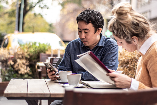 Mid adult man using mobile phone next to coworker in the coffee shop