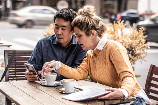 Mid adult man showing something on mobile phone to his coworker at coffee shop