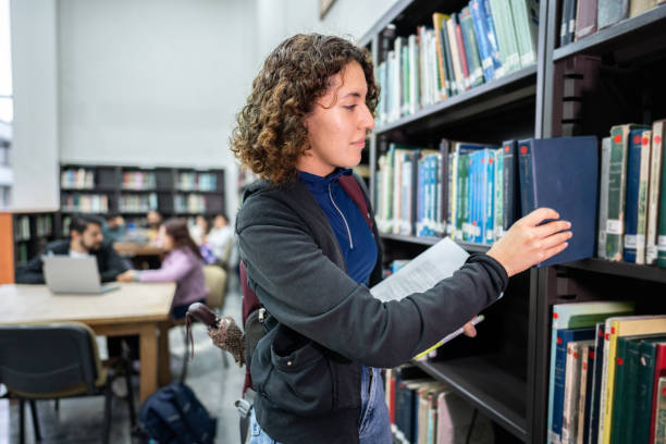 istock Young student looking for a book in the library bookshelf at the university 1494581058