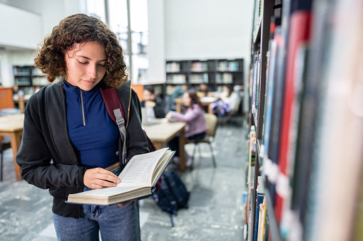 Young student woman reading a book on library in the university
