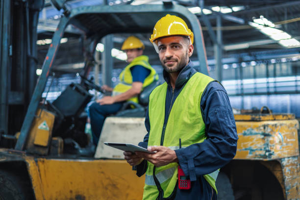 warehouse worker standing  look at camera and  forklift operator in factory