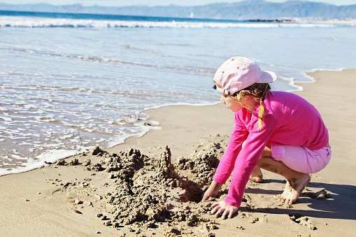 Young girl watches a wave approach her drippy castle