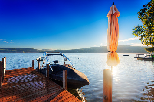 Early morning sun over the hills surrounding a New Hampshire Lake shines behind a furled umbrella on a wood dock