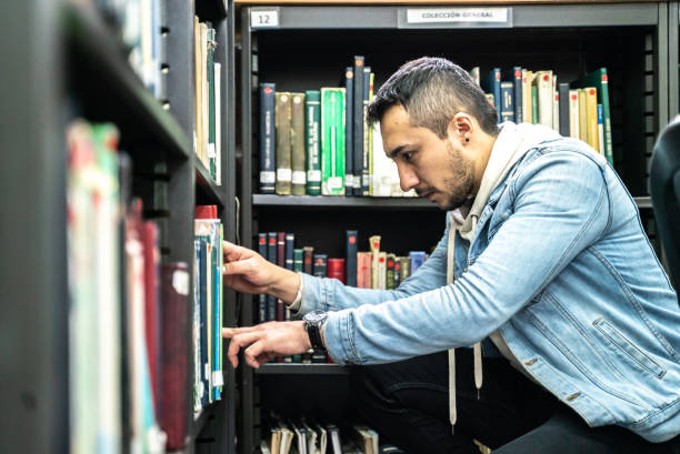 istock Young student looking for a book in the library bookshelf at the university 1494588905