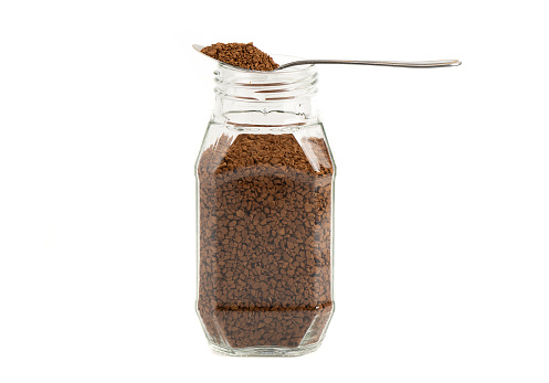 Spoon with granulated instant coffee on a glass jar with coffee. Isolated on white background with place for text.