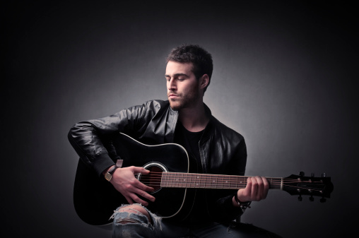 Handsome young man in leather jacket playing the guitar