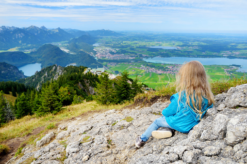 Cute little hiker enjoying picturesque views from the Tegelberg mountain, a part of Ammergau Alps, located near Fussen town, Bavaria, Germany.