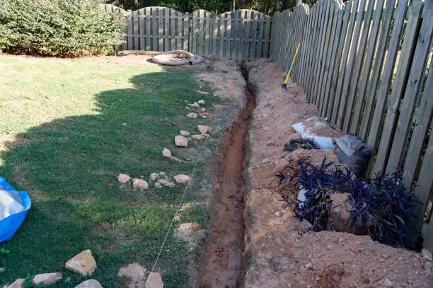 Trench excavated through a backyard of red clay for the DIY installation of a french drain.