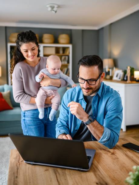 Family with a baby at home, Father using a laptop.