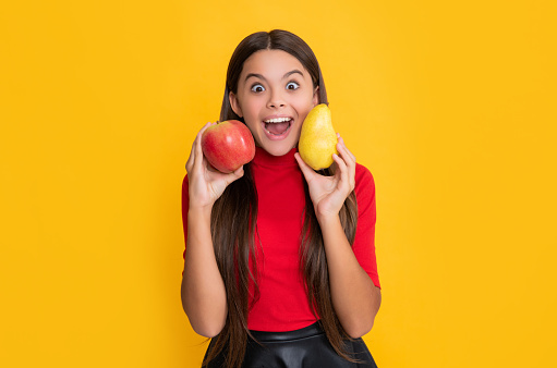 smiling surprised girl hold fresh apple and pear on yellow background.