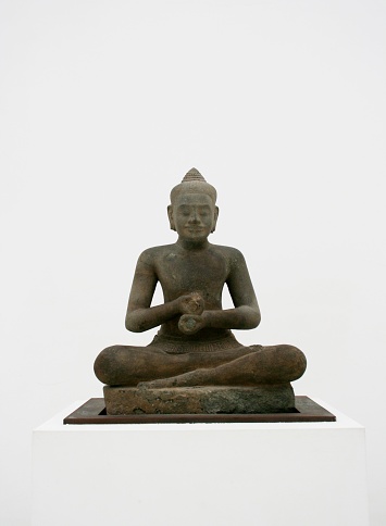 A bronze statue of a buddha kneeling in a meditative pose against a white background