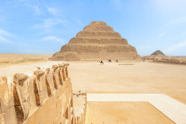 uomini che cavalcano cammelli alla piramide a gradoni, sakkara, egitto - saqqara foto e immagini stock