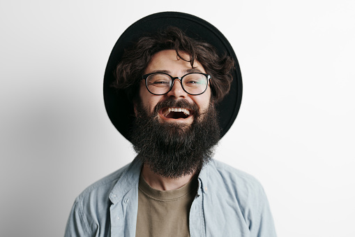 Handsome stylish man with beard on white background. Smiling man wearing black hat and glasses