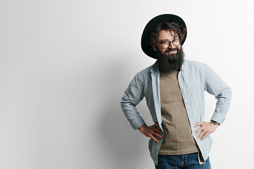 Handsome stylish man with beard on white background. Smiling man wearing black hat and glasses