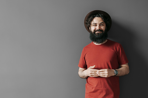 Handsome stylish man with beard on black background. Smiling man wearing black hat and red t-shirt
