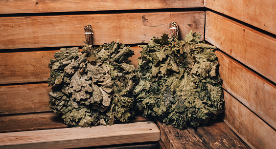 Brooms for steaming in the sauna are on a wooden shelf. Oak broom