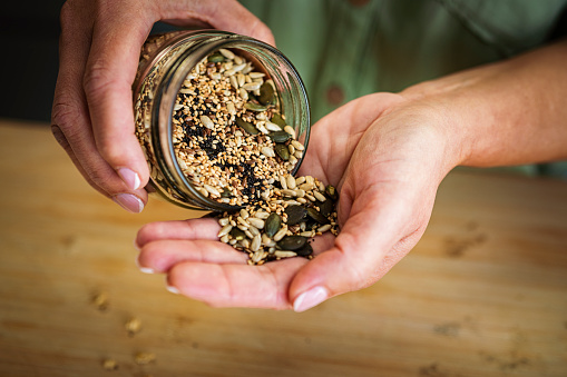 Woman scattering mixed seed on palm of hand from the jar