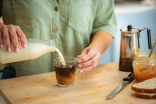 Cropped shot of a woman pouring vegan milk into a cup of black coffee