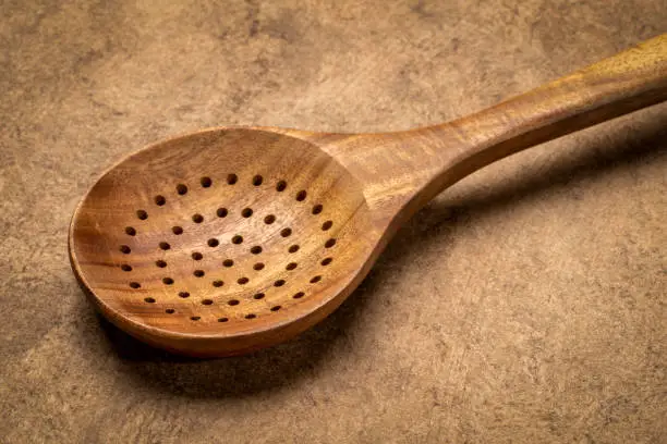 drainer spoon - wooden kitchen cooking utensils on textured bark paper