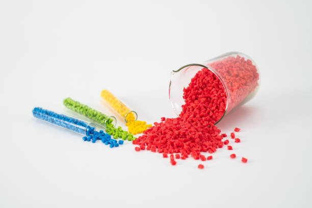 Creative composition of masterbatches, falling red granules from the beaker and blue, green, and yellow granules from the test tube on the white base, close-up shot.