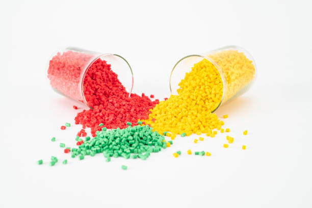 Stack of creative masterbatches, close-up shot of red and yellow plastic polymers falling from two beakers near green plastic placed on white base.