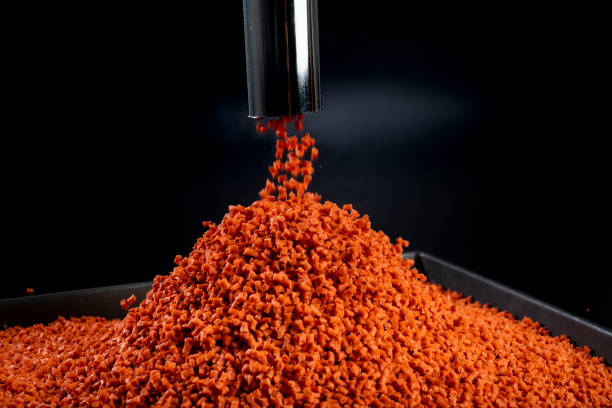 istock Creative shot of orange polymer granules falling through a metal pipe on a black tray with black background 1494617759