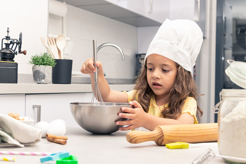 girl with apron and white pastry chef's hat, kneading dough in the kitchen, making pastry.