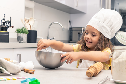 girl with apron and white pastry chef's hat practicing baking, mixing ingredients