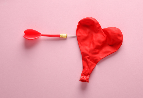 Dart and inflates red heart shaped balloon on pink background. Love concept