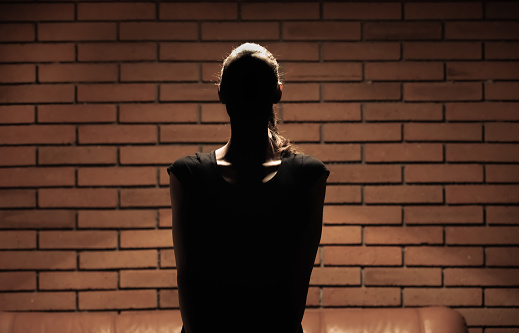 Woman standing in the shadow against brick wall.