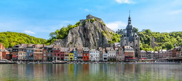 Colorful image with buildings and citadel along the Meuse river in Dinant, Wallonia, Belgium. Reflection of houses in the water. Panoramic travel image.