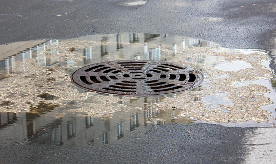 Metal hatch, drain drain. Water near the manhole on the street.