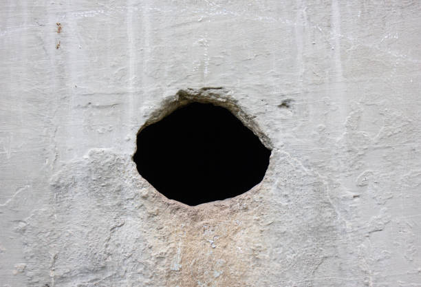 Hole in a concrete wall. Gray concrete wall with a through hole.Split, crack and black hole in a concrete wall. Damage from natural disasters. Catastrophe. Damage to the wall, concrete structure.