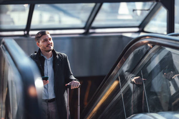 Smiling Businessman Using A Mobile Phone While Riding Escalator At Subway Station