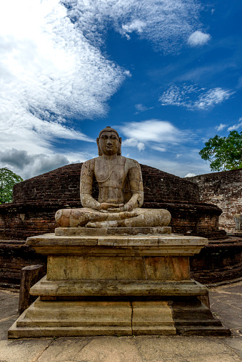 The stone buddha statue sits in meditation in front of the stone steps of the Vatadage temple in Polonnaruwa, Sri Lanka.