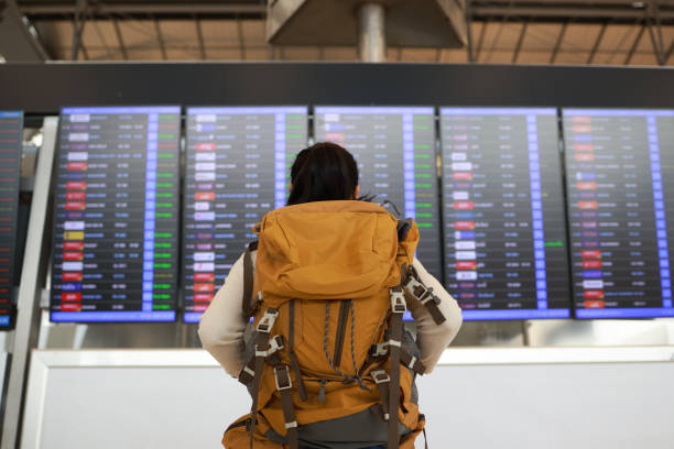 istock ackview female tourist with orange backpack check flight on Flight Information board in airport ,Travel, airport and excited woman with passport. travel ticket and documents for immigration, journey and flight schedule. 1494636509