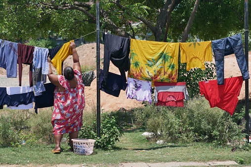 Trincomalee, Sri Lanka – 04.17.2022: A fat woman hangs her laundry on lines strung up alongside the road during the island’s economic crisis