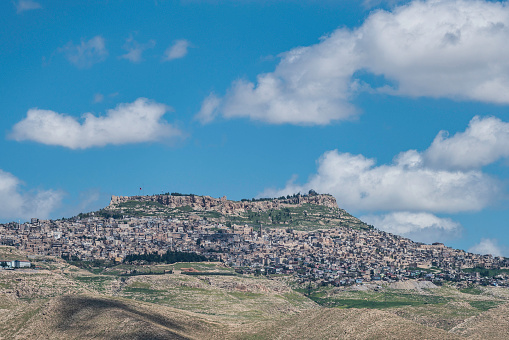 Historical Mardin city view, built on the top of the mountain. The city is photographed from the lower angle, including the cloudy sky. Shot with a full-frame camera during the day.