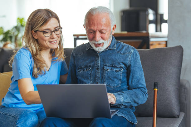 istock Active senior man using laptop with female carer sitting by on sofa at home 1494643871