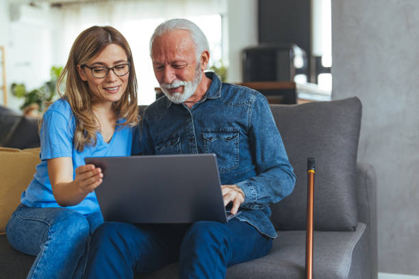 istock Active senior man using laptop with female carer sitting by on sofa at home 1494643908