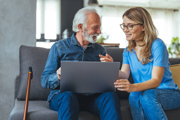 istock Active senior man using laptop with female carer sitting by on sofa at home. 1494643963