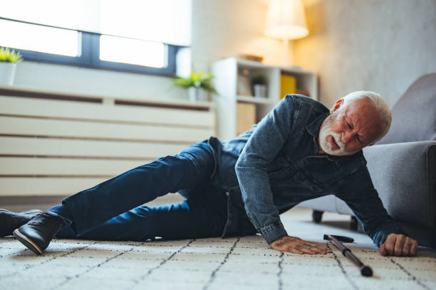 Old man suffering with pain and struggling to get up after falling down at home A Senior Man who is Using a Walking Stick is Lying on the Wooden Floor in his Apartment After he Fell in Serious Accident. Senior man lying on the floor of his room in an assisted living home standing had to knee pose stock pictures, royalty-free photos & images