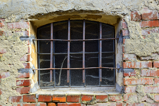 Old, dirty and barred window - an old window in a battered brick wall