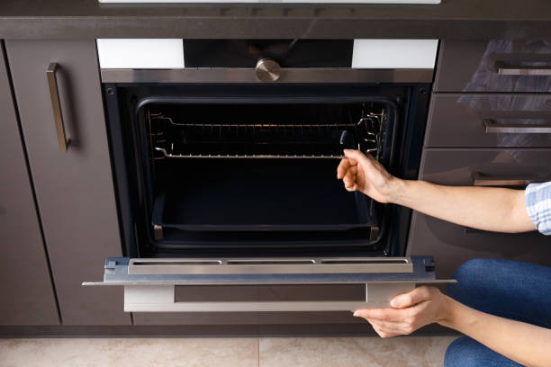 uma menina abre a porta de um forno embutido com uma exibição em um interior de cozinha moderna. - home interior women domestic kitchen cabinet - fotografias e filmes do acervo