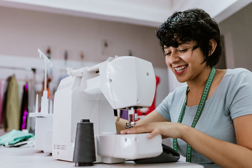 Young latin woman fashion designer working with a sewing machine at her workshop in Mexico Latin America, Hispanic small business owner female